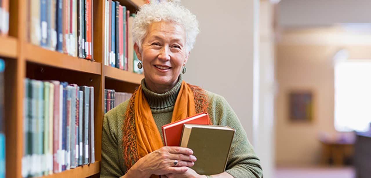 Une femme d’âge mûr tient des livres dans une bibliothèque